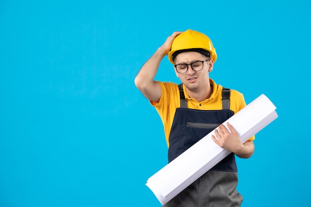 Front view stressed male builder in uniform with paper plan on blue 