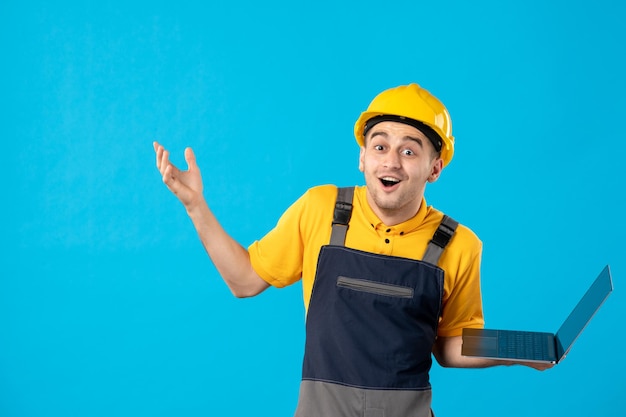 Vista frontale del lavoratore maschio sorpreso in uniforme con il computer portatile sull'azzurro