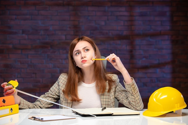 front view thinking female worker in construction site holding tape measure and writing notes agenda engineer corporate project business job plan manager