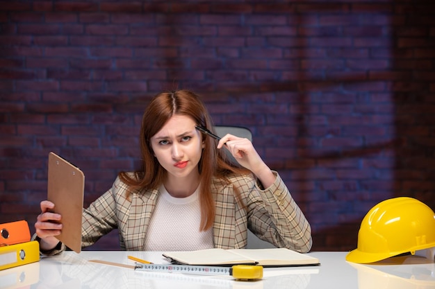 Фото Вид спереди думающая женщина на стройке сидит за столом с документами работа корпоративный подрядчик план проекта менеджер инженер