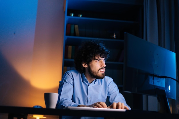 Front view of thoughtful man looking away and starts typing on wireless keyboard while sitting at desk