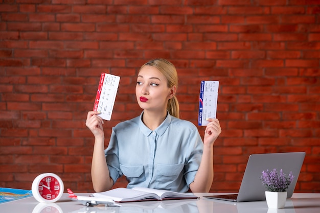 Photo front view of travel agent sitting behind her working place holding tickets global manager agency map indoors service tourism assistant flight