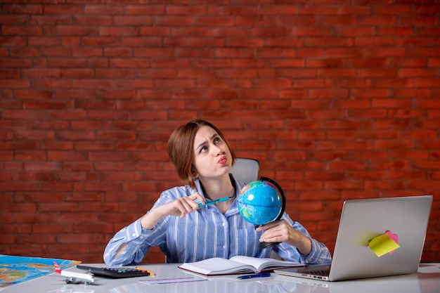 Front view travel agent sitting behind her working place with little globe assistant agency map indoors operator service manager