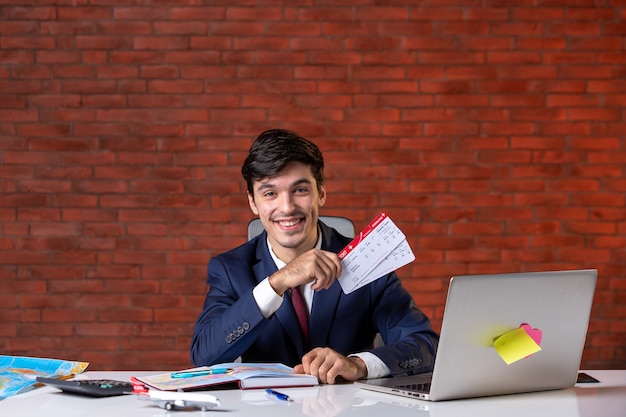 front view of travel agent sitting behind his working place in suit holding pair of tickets overseas corporate occupation global assistant job project service