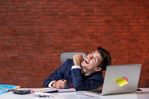 Photo front view of travel agent sitting behind his working place in suit and taking notes corporate occupation global tourism overseas agency project service