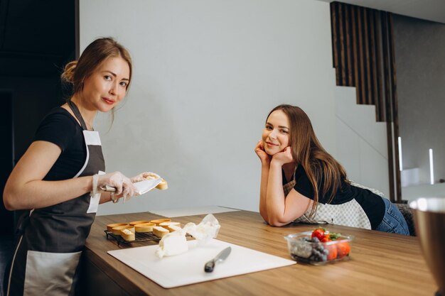 Front view of two confectioners cooking desserts Beautiful women wearing white and black uniform They holding confectionery bags and putting dough on baking sheet