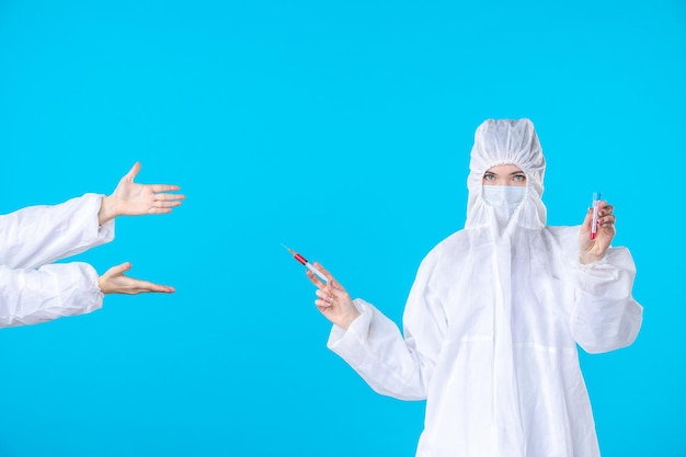 Photo front view two female doctors in protective suit and mask one holding injection on a blue background medical covid- virus health science hospital pandemic