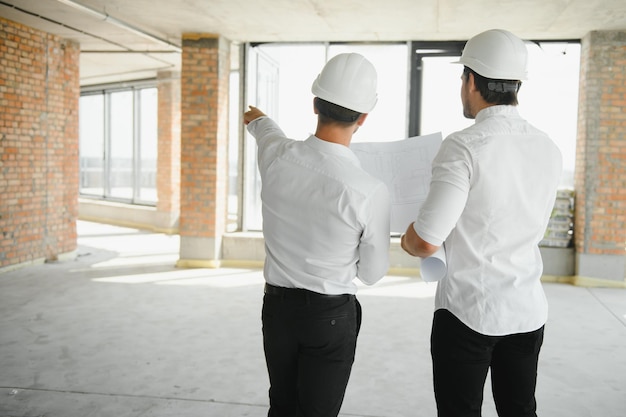 Foto una vista frontale di due architetti intelligenti con caschi bianchi che esaminano i progetti in un cantiere in una luminosa giornata di sole