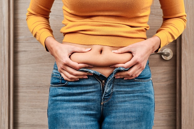 Foto vista frontale di una donna grassa irriconoscibile che mostra la sua vita per vedere il suo peso in eccesso.