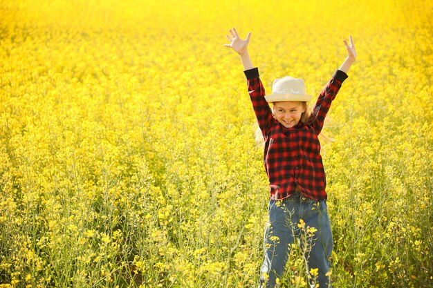 Front view van klein kind meisje met hoed kijkt naar de camera til je handen omhoog in bloeiende koolzaad