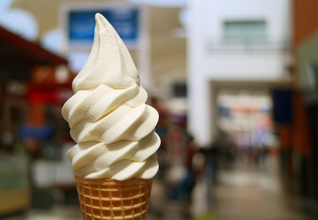 Front view of vanilla milk soft serve ice cream cone in the sunlight, with blurred city center view in background