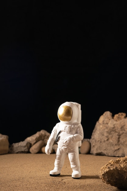 Front view of white astronaut around stones on black