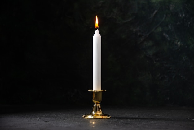 Front view of white candle in golden stand on the black