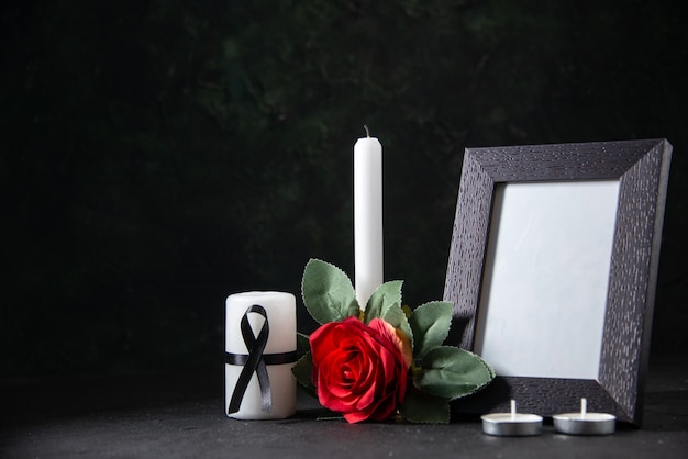 Front view white candle with picture frame and flower on a dark surface