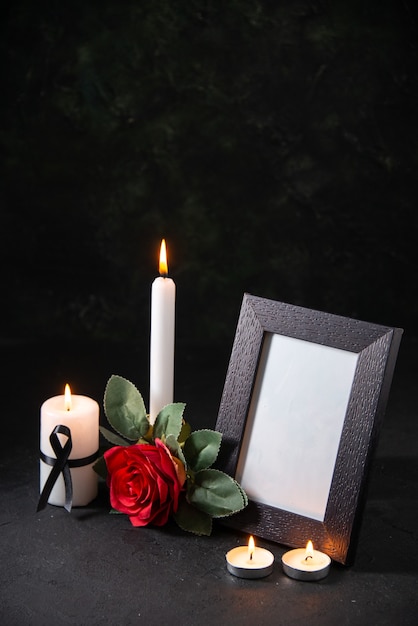 Front view white candle with picture frame and flower on dark surface