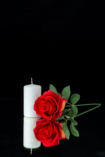 Front view of white candle with red rose on black