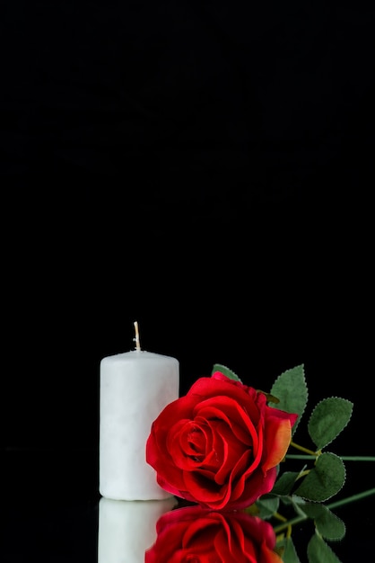 Front view of white candle with red rose on black