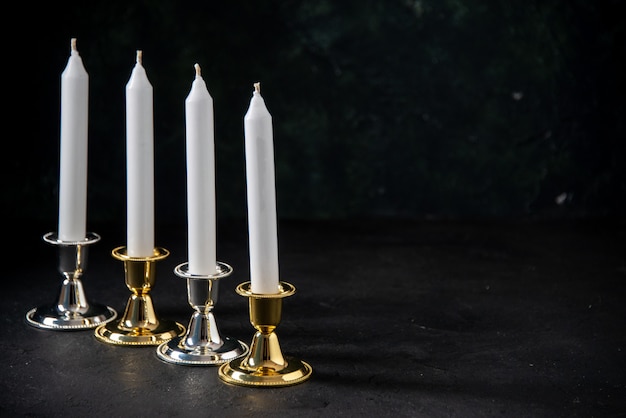 Вид спереди белых свечей в золотой и серебряной подставке на черном