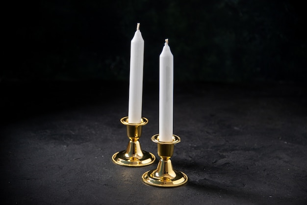 Front view of white candles in golden stand on black