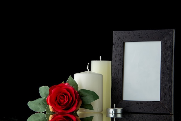 Front view of white candles with picture frame on the black wall