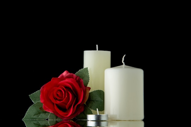 Vista frontale di candele bianche con fiori rossi su parete nera