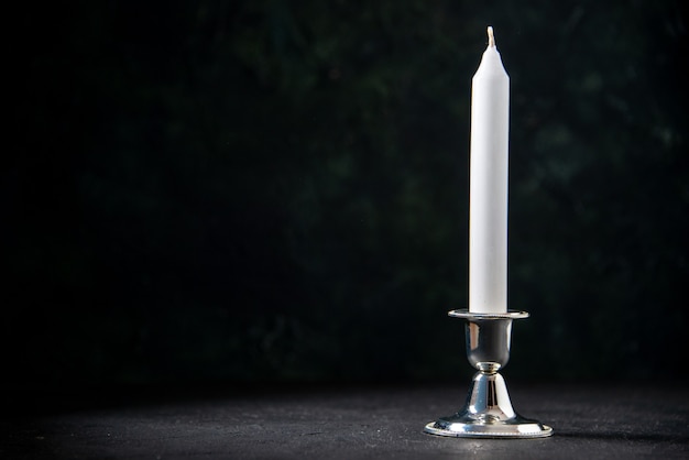 Front view of white long candle on dark wall