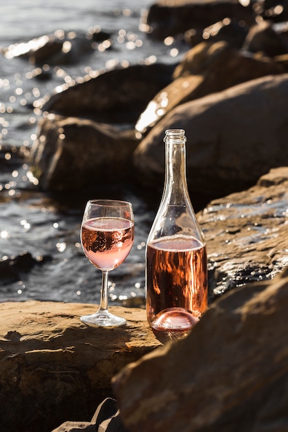 Bicchieri di vino e bottiglia di vista frontale sulle rocce dell'oceano