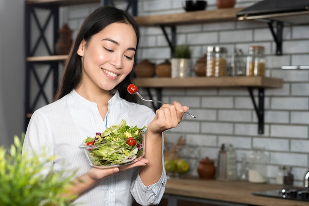 Foto vista frontale della donna che mangia pomodoro ciliegia con verdure verdi