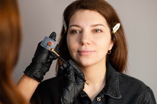 Front view of woman getting an eyebrow treatment from female beautician