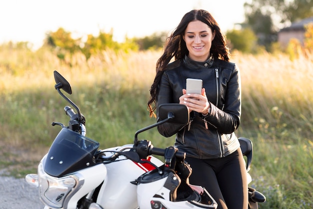 Foto vista frontale della donna che guarda lo smartphone mentre è appoggiato alla sua moto