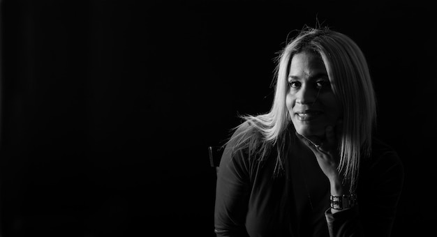 Front view of a woman sitting on a chair smiling and looking at camera black background