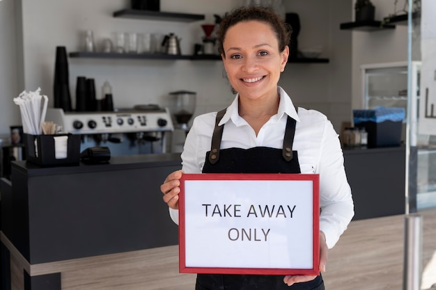 Photo front view of woman wearing apron holding sign with takeaway only