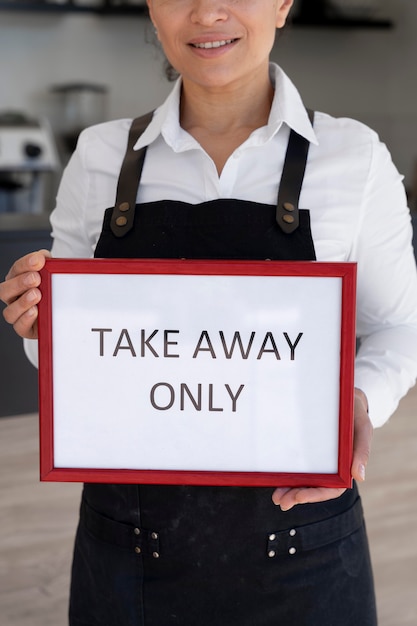 Photo front view of woman wearing apron holding sign with takeaway only