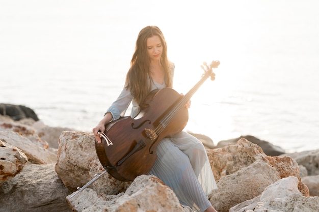 Vista frontale della donna con il violoncello sulle rocce