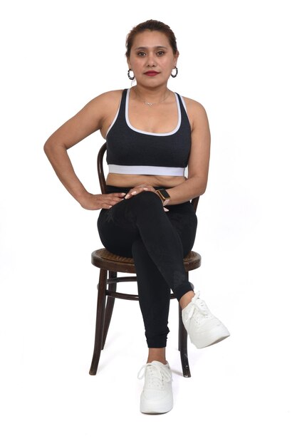 Front view of women sitting on chair with sportswear looking at camera hand on hip on white background