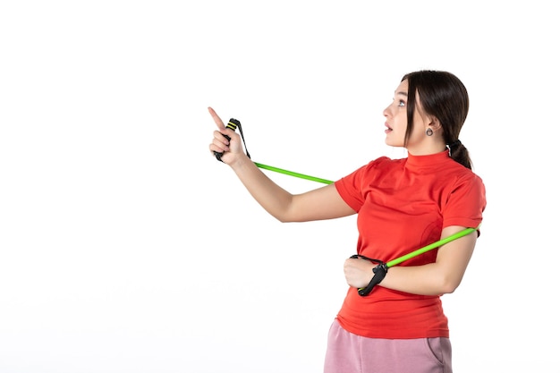 Front view of a wondering young woman neatly gathering her hair dressed in redorange blouse and holding rope sport accessory pointing up on white background