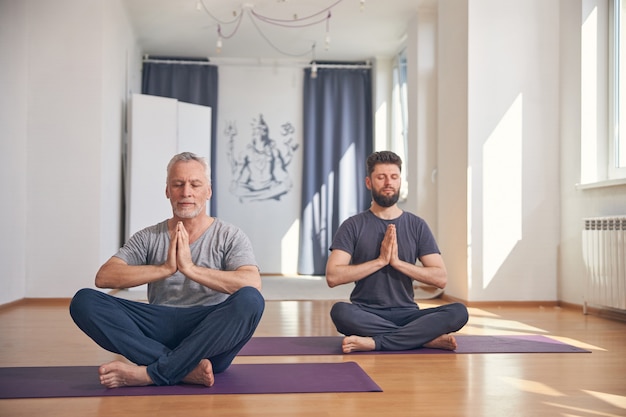 Front view of yogis sitting with clasped hands in a lotus pose during the workout