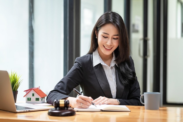 Front view of young Asian businesswoman or lawyer holding pen to note real estate consulting ideas the mallet is placed at the tablexA