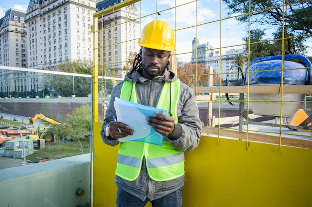 front view of young black engineer man and construction site manager reading document outdoors