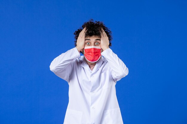 Front view young doctor in medical suit with red mask on blue background drug covid- pandemic medicine hospital virus vaccine health