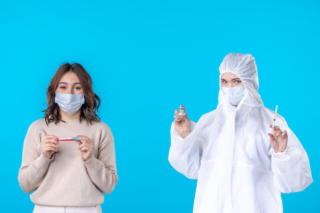 Vista frontale giovane dottoressa in tuta protettiva con paziente su sfondo blu scienza malattia virus medico covid- pandemia isolamento sanitario