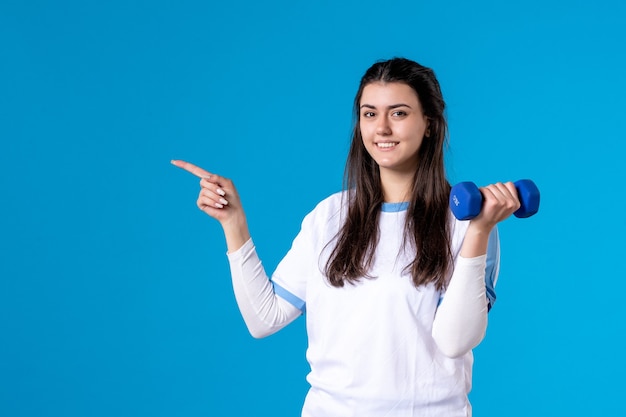 Front view young female holding blue dumbbells on blue wall