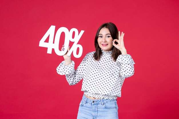 front view of young female holding discount on red wall