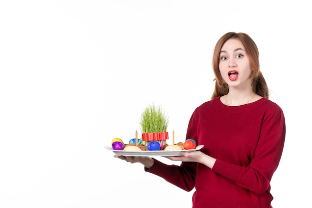 白い背景の上のセメニとノウルーズのお菓子とホンカを保持している若い女性の正面図コンセプトパフォーマー休日民族色民族春