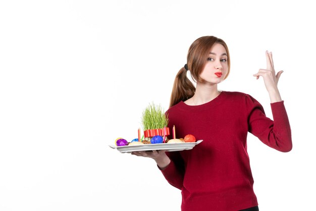 正面図白い背景の上のsemeniとnovruzのお菓子とhoncaを保持している若い女性エスニックパフォーマー民族休日春の色家族の概念