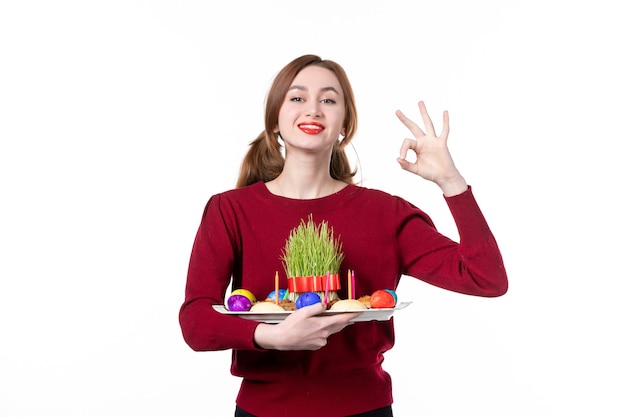 front view of young female holding honca with semeni and novruz sweets on white background holiday ethnicity ethnic spring performers colours concept