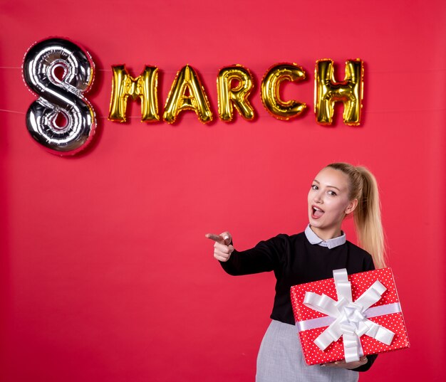 front view young female holding present with march decoration pointing on a red background passion womans day luxurious equality feminine shopping