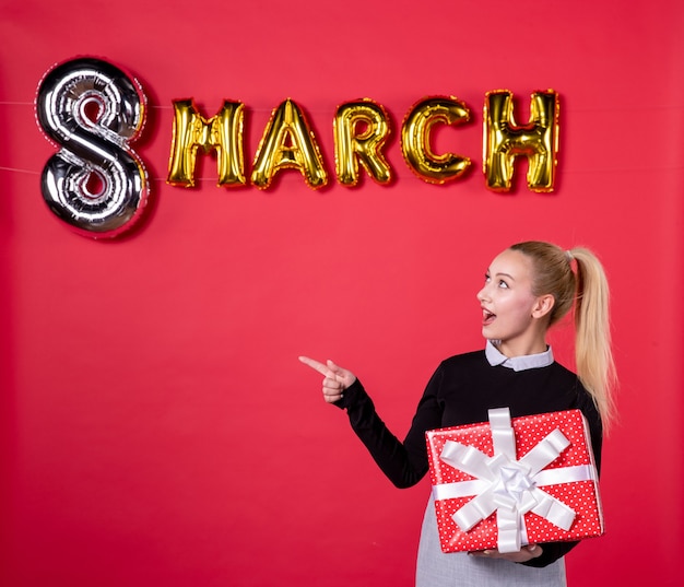 front view young female holding present with march decoration on red background passion salon womans day equality shopping money luxurious