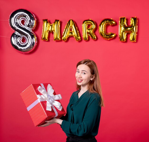 front view young female holding present with march decoration on red background vogue gift love woman womans day glamour feminine holiday