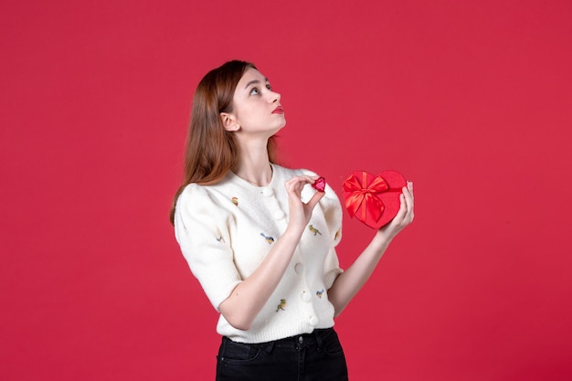 front view young female holding red heart shaped present on red background marriage womens day sensual march equality fashion shopping love